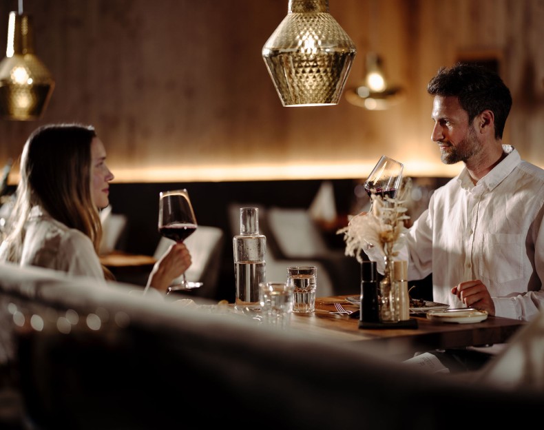 Paar genießt das Essen im Restaurant 1774 in Flachau und stößt mit Rotweingläsern an