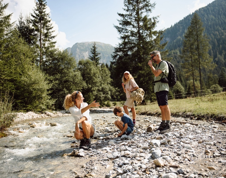 Eine Familie wandert durch die Berge Flachaus und stoppt an einem Bach