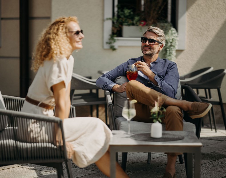 Paar sitzt entspannt auf der Terrasse und genießt Drinks in der Sonne