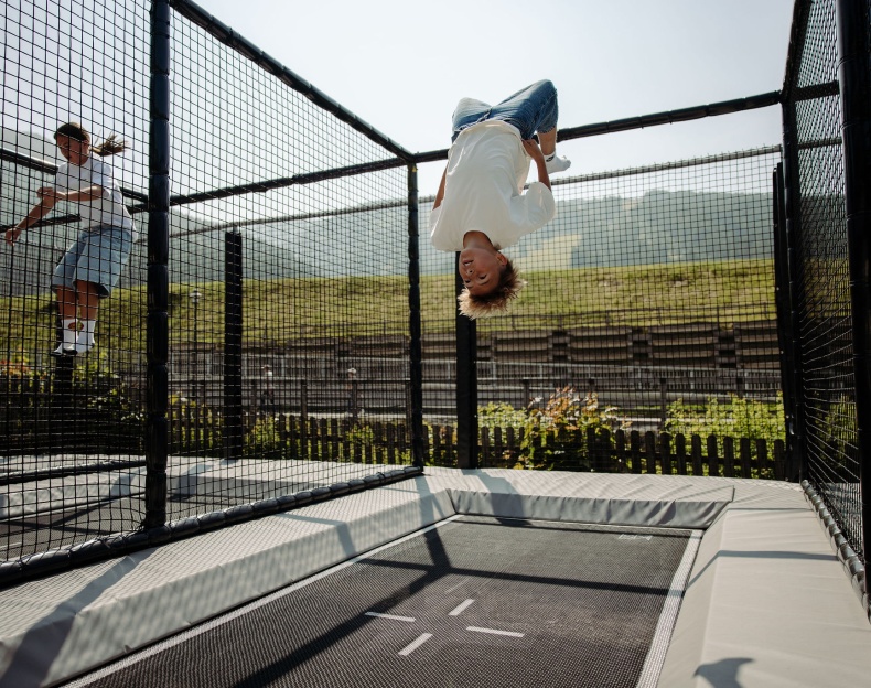 Zwei Kinder springen auf einem gesicherten Outdoor-Trampolin im Freien im Familienhotel Resl