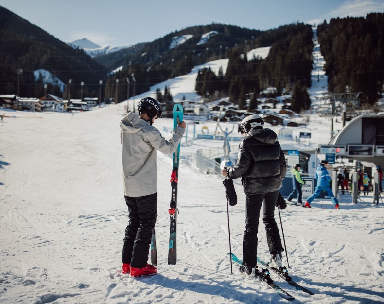 Zwei Skifahrer stehen auf einer verschneiten Piste mit Skilift im Hintergrund in Flachau, Ski amadé