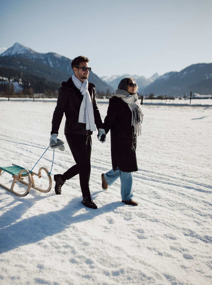 Ein Paar läuft im Schnee mit einem Schlitten vor der malerischen Bergkulisse Flachaus