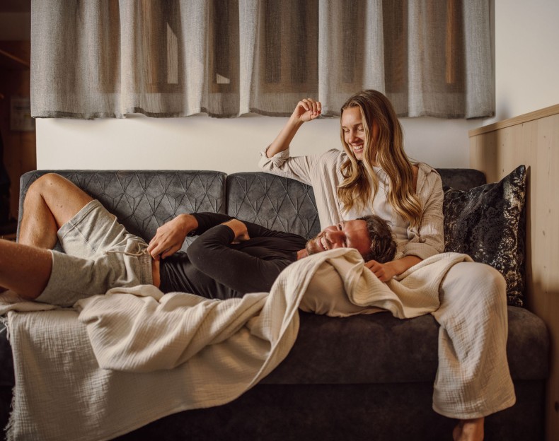 Paar liegt lächelnd auf einem Sofa, in Decken gewickelt