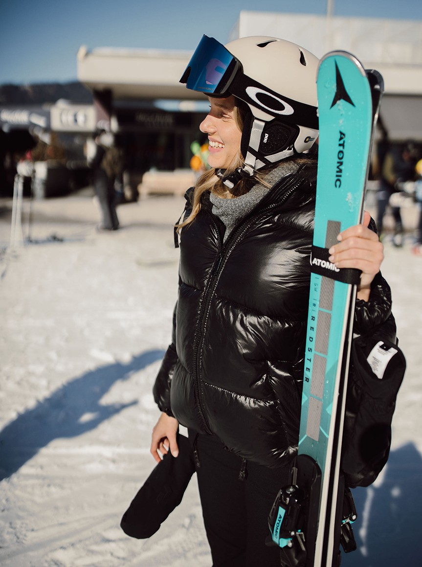 Eine Frau in Skikleidung lächelt und hält ein Paar Skier in der Hand 