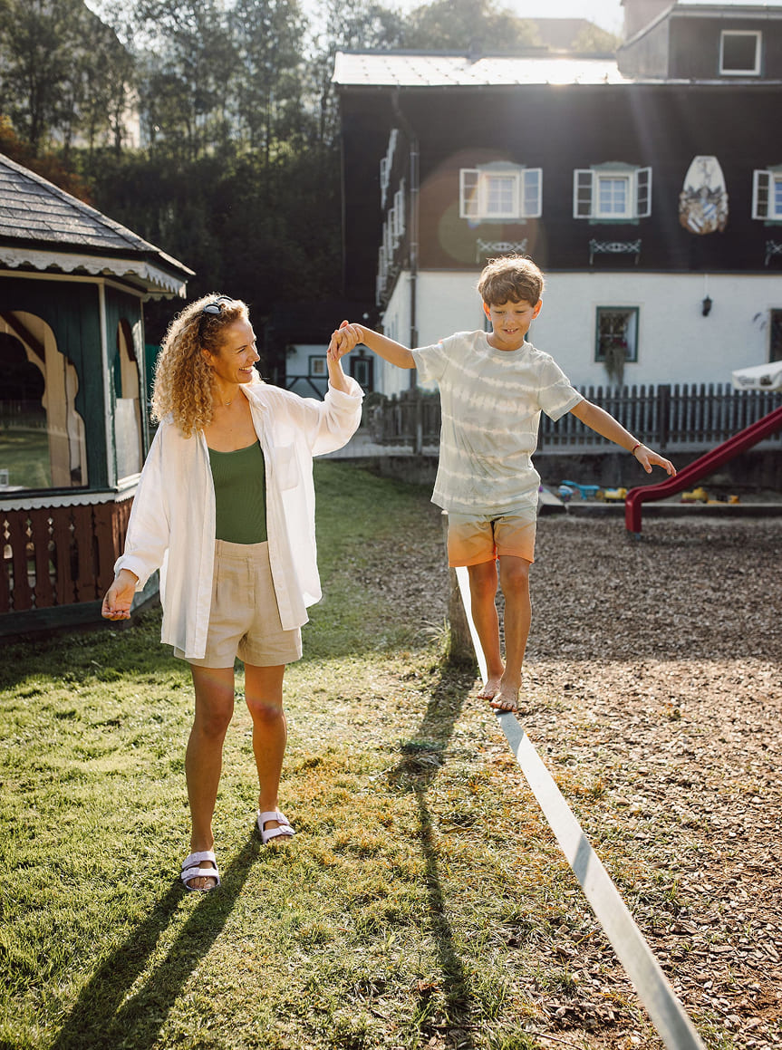 Eine Frau hält die Hand eines Jungen, der auf einem Spielplatz balanciert