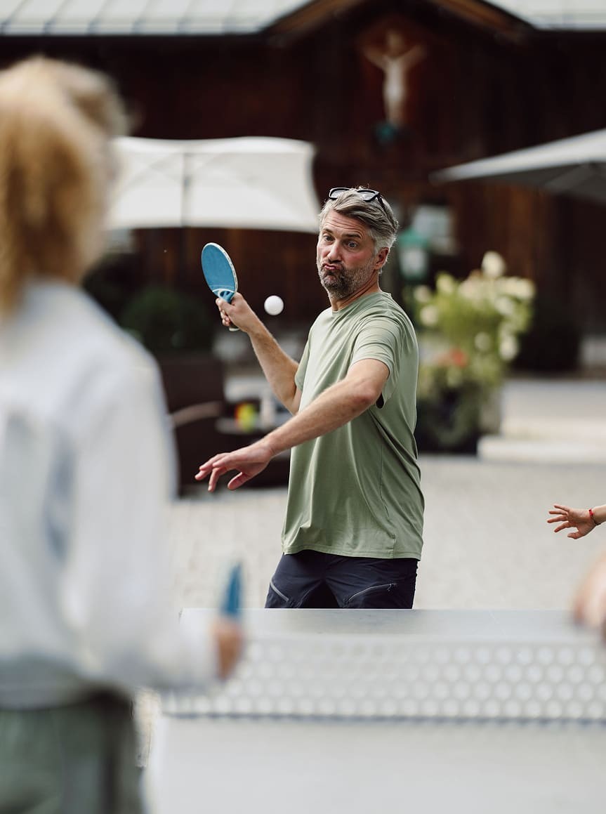 Ein Mann in grünem T-Shirt spielt Tischtennis im Freien mit seiner Familie