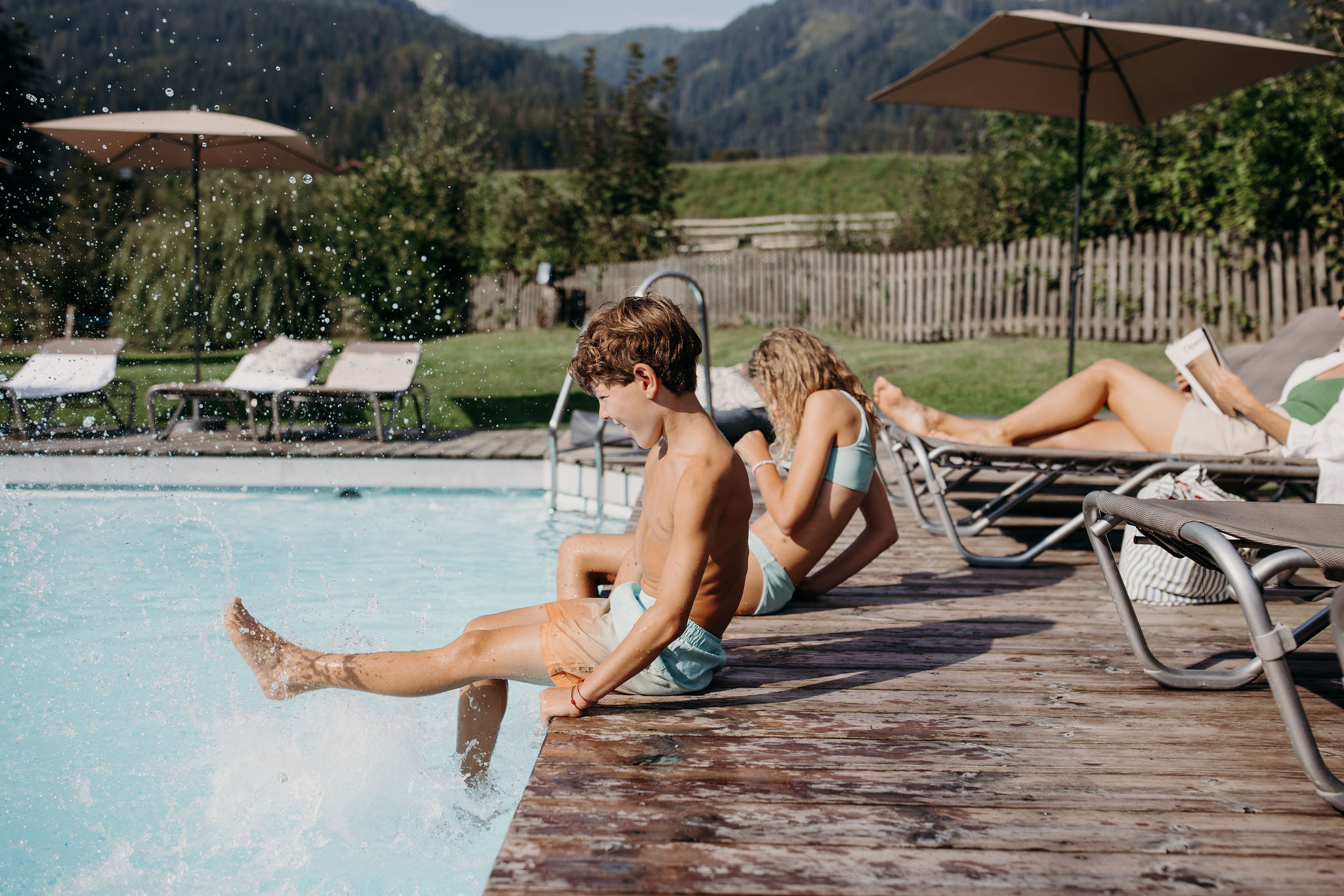 Kinder spritzen am Pool, während Erwachsene sich auf Liegen entspannen
