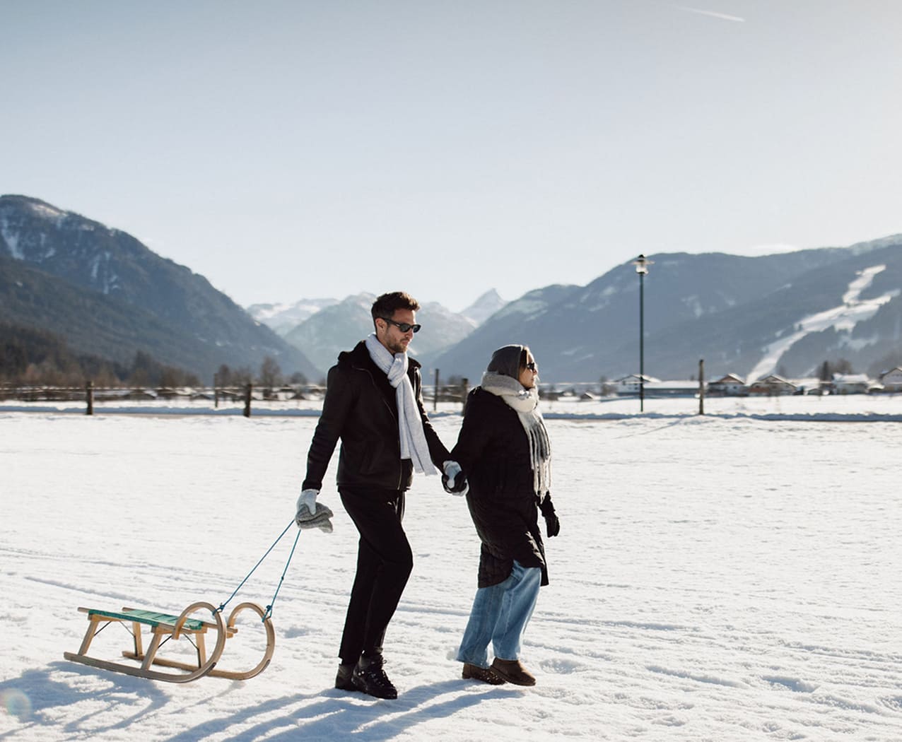 Pärchen macht einen romantischen Winterspaziergang in Flachau mit Schlitten auf einer verschneiten Wiese.