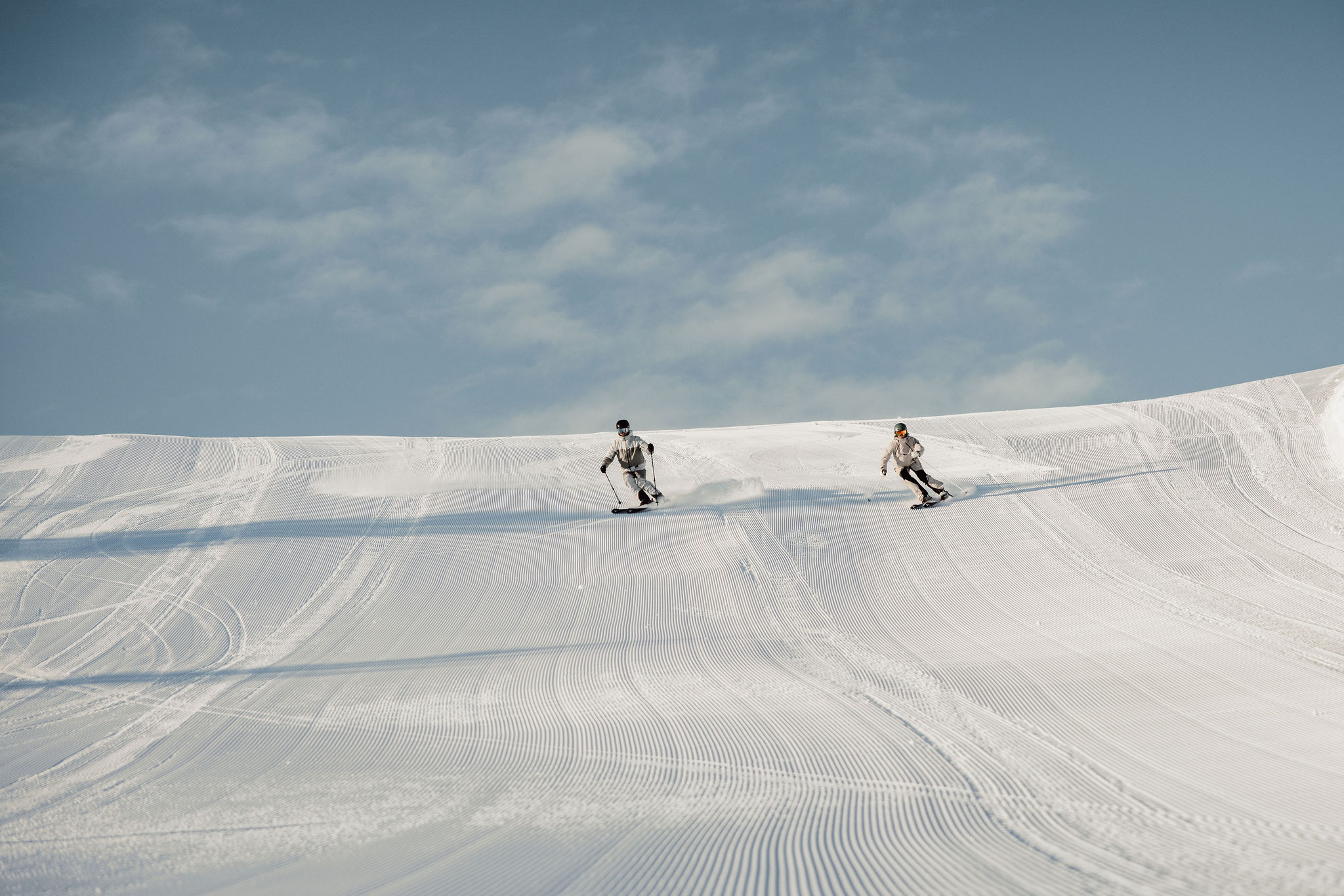 Zwei Snowboarder fahren nebeneinander auf einer frisch präparierten Piste bei klarem Himmel