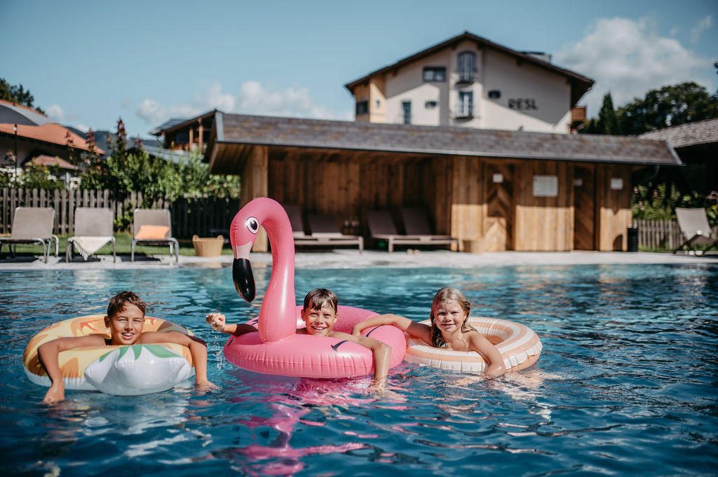 Kinder schwimmen auf aufblasbaren Ringen in einem Pool vor einem Holzgebäude