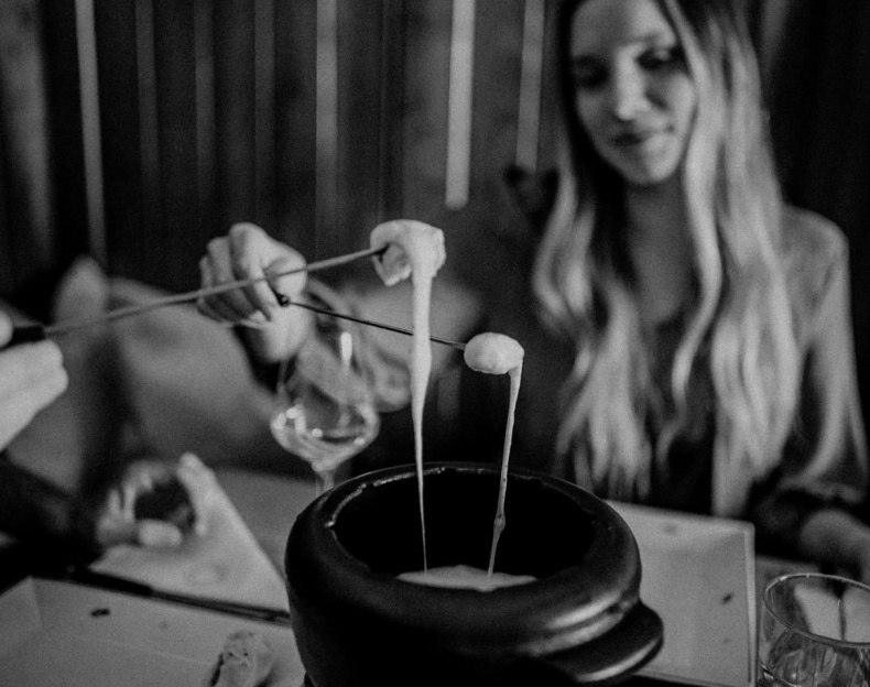 Frau genießt Käsefondue im Restaurant Ennshof in Flachau, Käse wird mit Brot auf Fonduegabeln aus dem Topf gezogen