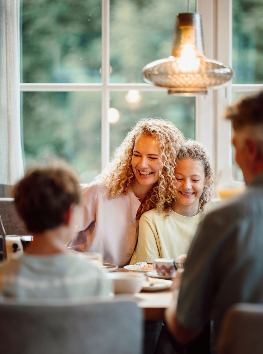 Familie sitzt glücklich zusammen am Frühstückstisch vor einem großen Fenster
