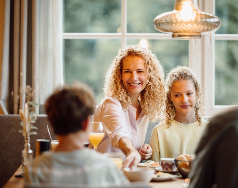 Familie sitzt glücklich zusammen am Tisch beim Frühstück vor einem großen Fenster