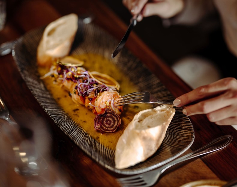 Person schneidet Garnelengericht mit Brot auf einem schicken Teller