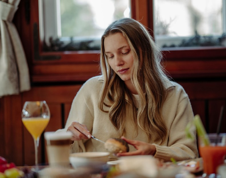 Frau isst am Frühstückstisch mit einem Glas Orangensaft und einer Kaffeetasse
