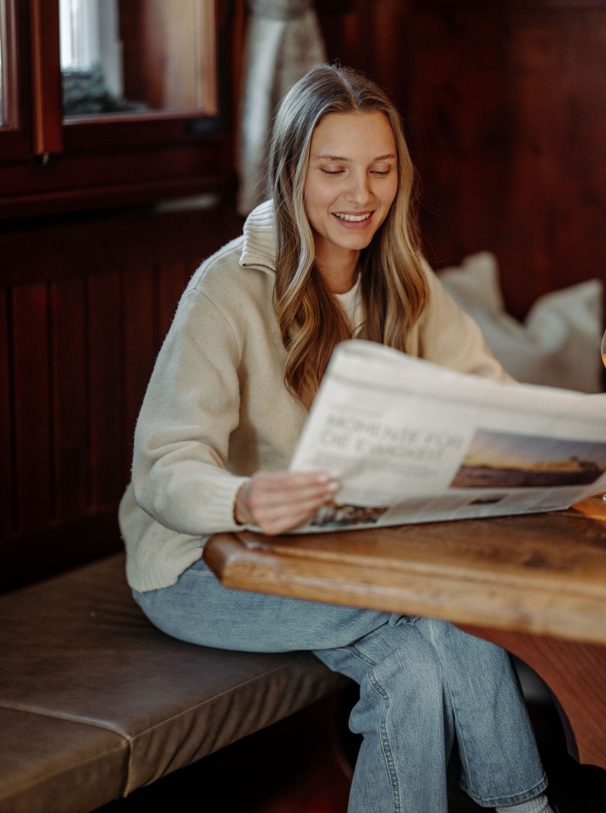 Eine Frau sitzt lächelnd am Frühstückstisch und liest die Zeitung.