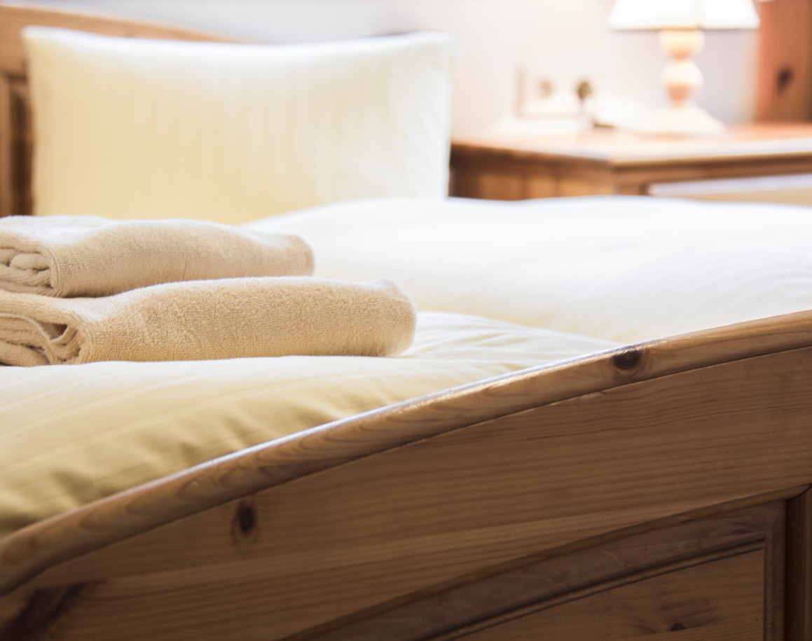Beige Handtücher liegen auf einem holzgerahmten Bett mit weißer Bettwäsche