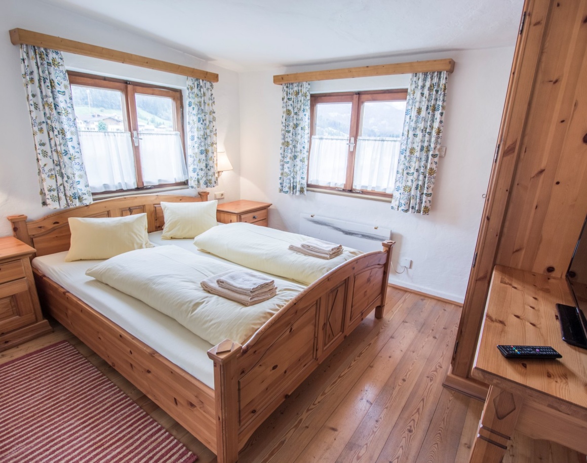 Gemütliches Schlafzimmer mit Holzmöbeln und Fenstern mit geblümten Vorhängen