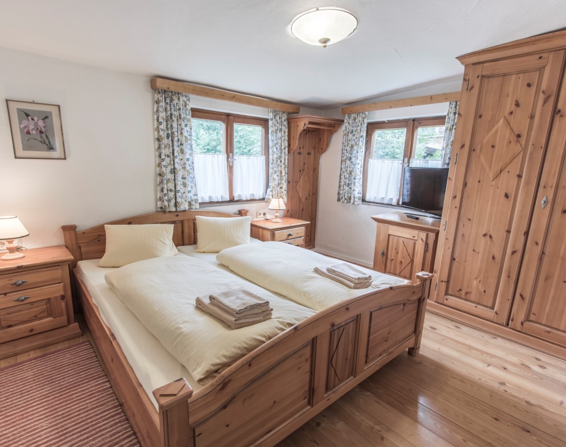 Helles Schlafzimmer mit Holzbetten, Schränken und zwei Fenstern mit Vorhängen