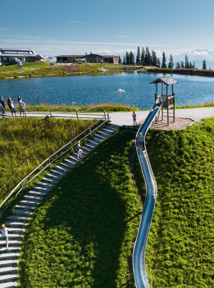 Kind spielt auf einer Rutsche neben einem Bergsee mit Blick auf die Berge