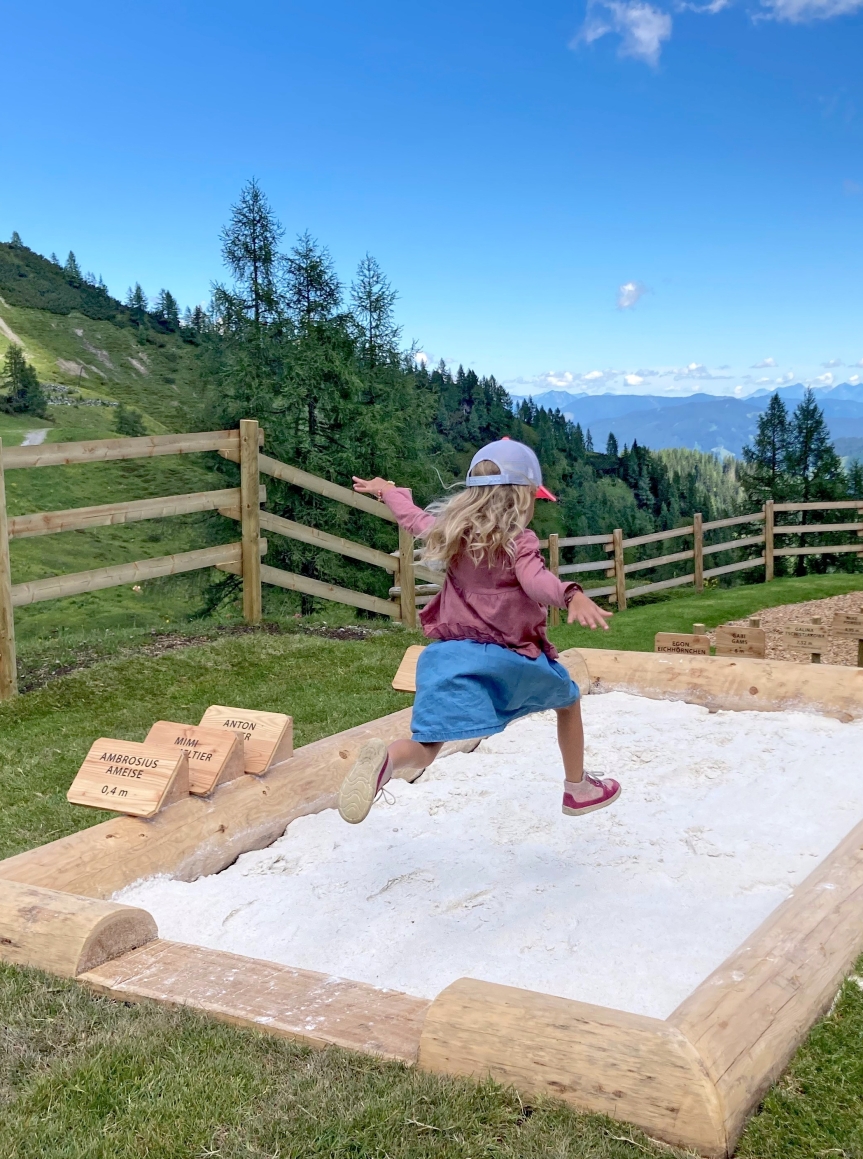 Kind springt in eine Sandkiste am Berg