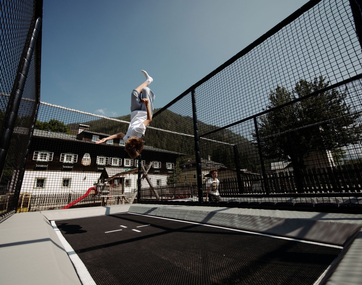 Kind springt auf der gesicherten Outdoor-Trampolinanlage im Hotelgarten