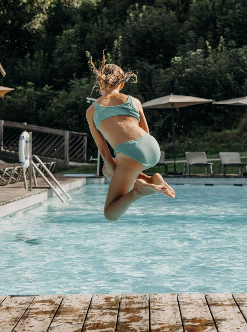 Mädchen springt in einen Pool bei sonnigem Wetter.