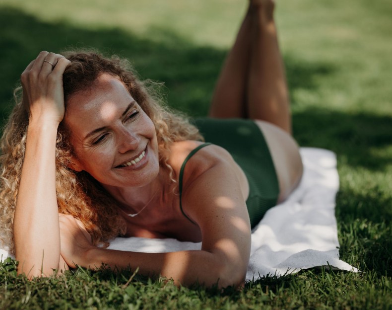 Eine Frau liegt lächelnd auf einer Decke im Gras und genießt die Sonne