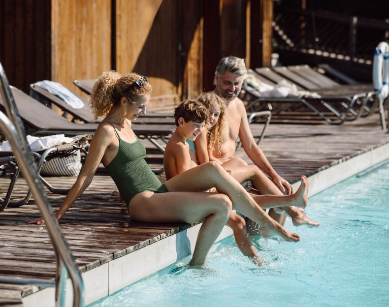 Eine Familie sitzt am Poolrand und planscht mit den Füßen im Wasser