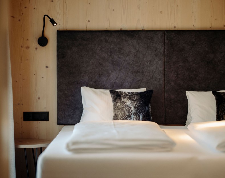 Modernes Hotelzimmerbett mit schwarzem, gepolstertem Kopfteil und eleganter Beleuchtung