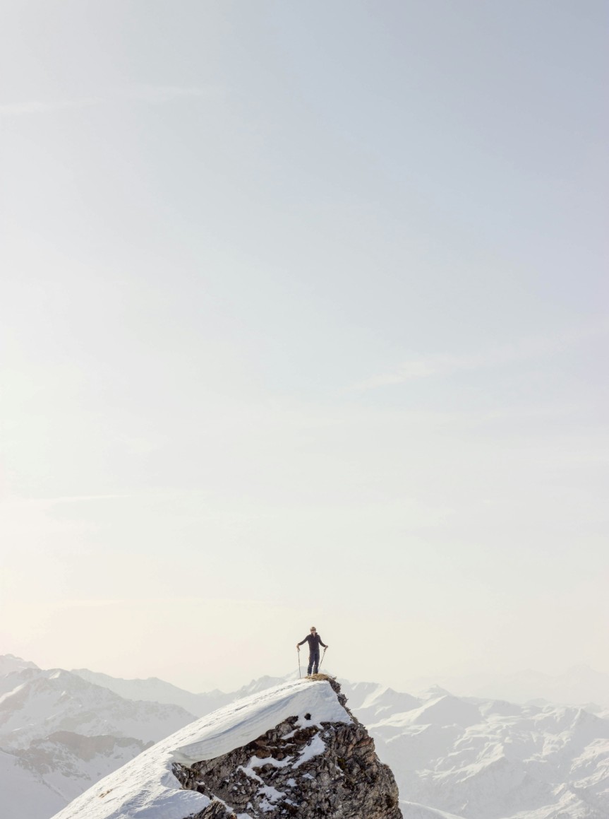 Eine Person steht mit Skistöcken auf einem verschneiten Berggipfel © Haut Risque auf Unsplash
