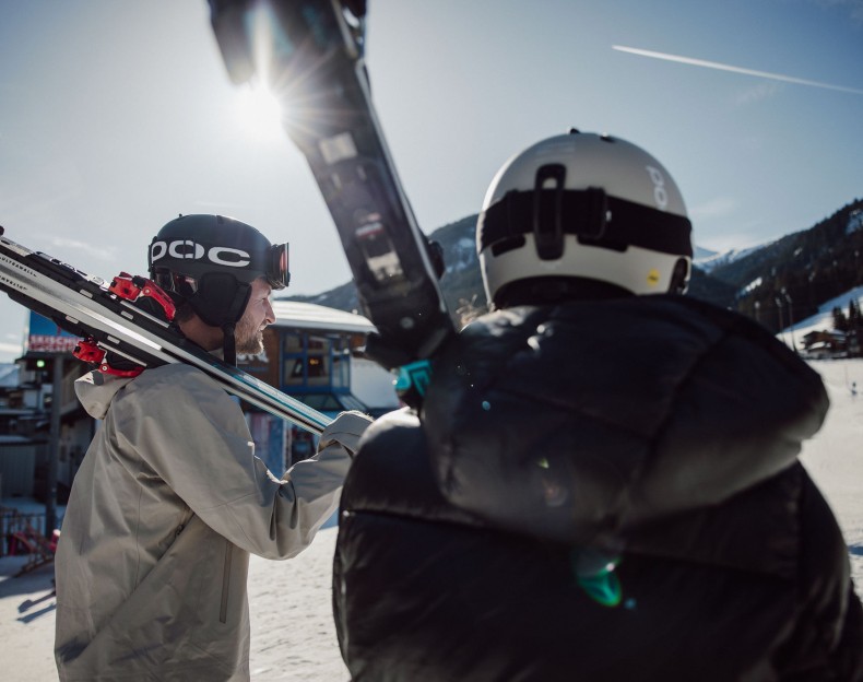 Wintersportler trägen ihre Ski, während die Sonne im Snow Space Salzburg strahlt