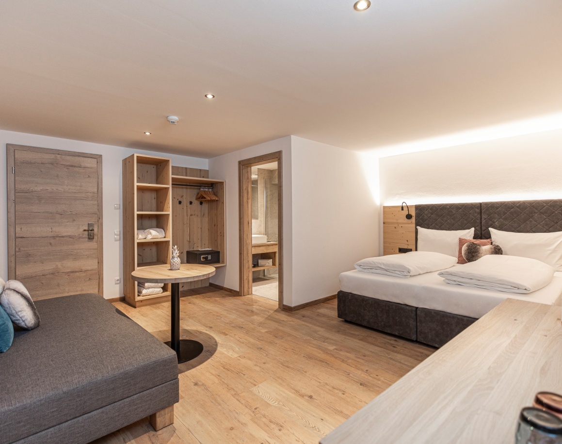 Hotelzimmer mit Doppelbett, offener Garderobe und Holzboden