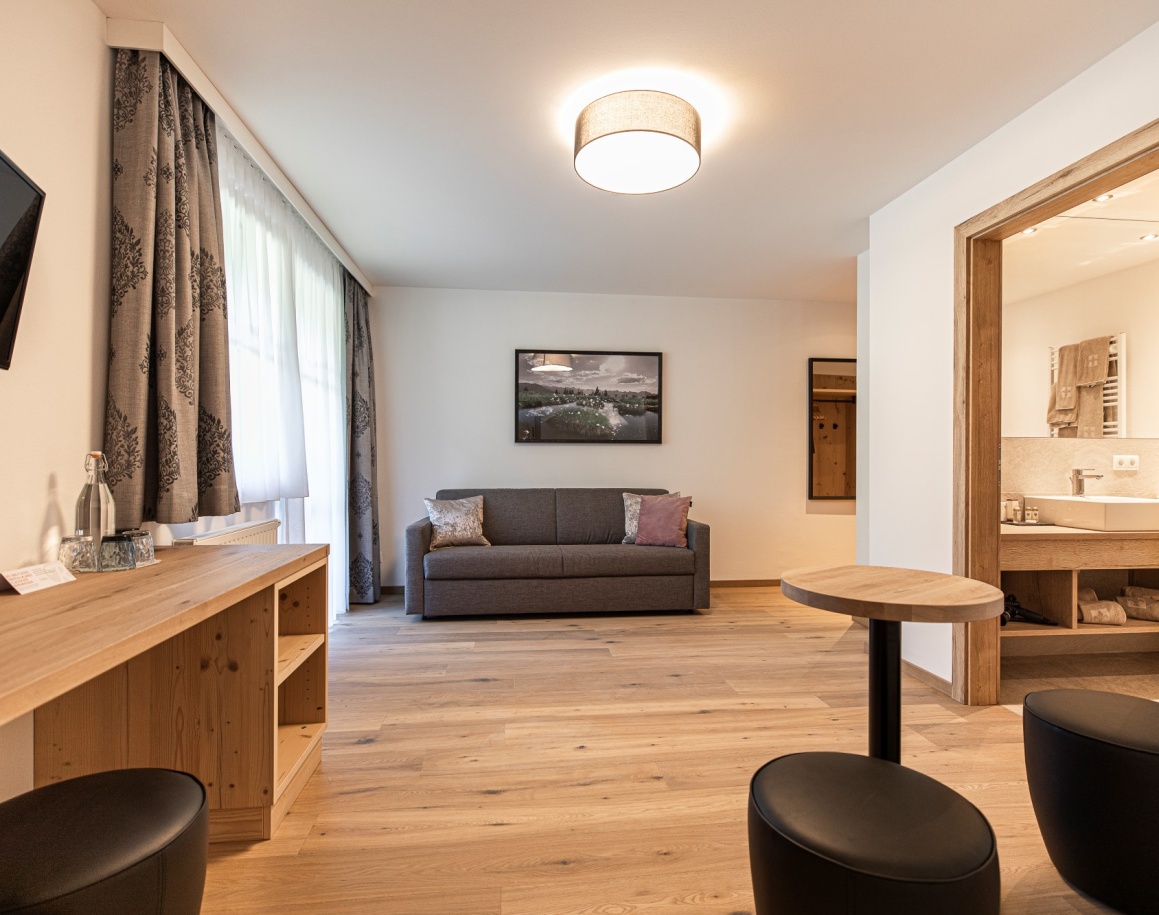 Helles Wohnzimmer mit grauem Sofa, Holzboden und Zugang zu modernem Bad