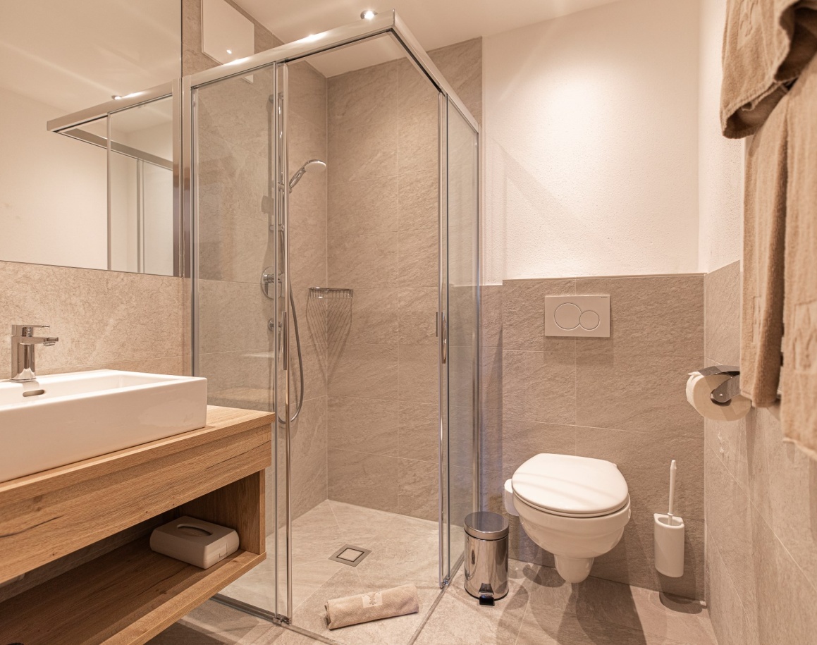 Modernes Badezimmer mit Dusche, Waschbecken und Toilette auf hellen Fliesen