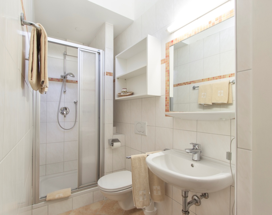 Helles Badezimmer mit Dusche, WC und Waschbecken, beige Fliesen und Handtüchern