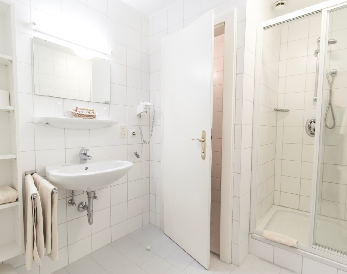 Helles Bad mit Waschbecken, Spiegel, Dusche und weißen Fliesen