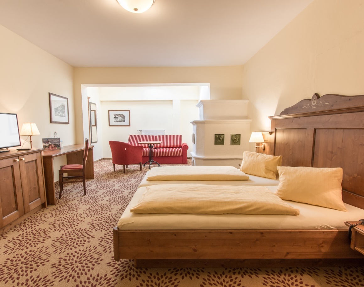 Helles Hotelzimmer im Ennshof mit Doppelbett, Schreibtisch und rotem Sofa im Hintergrund