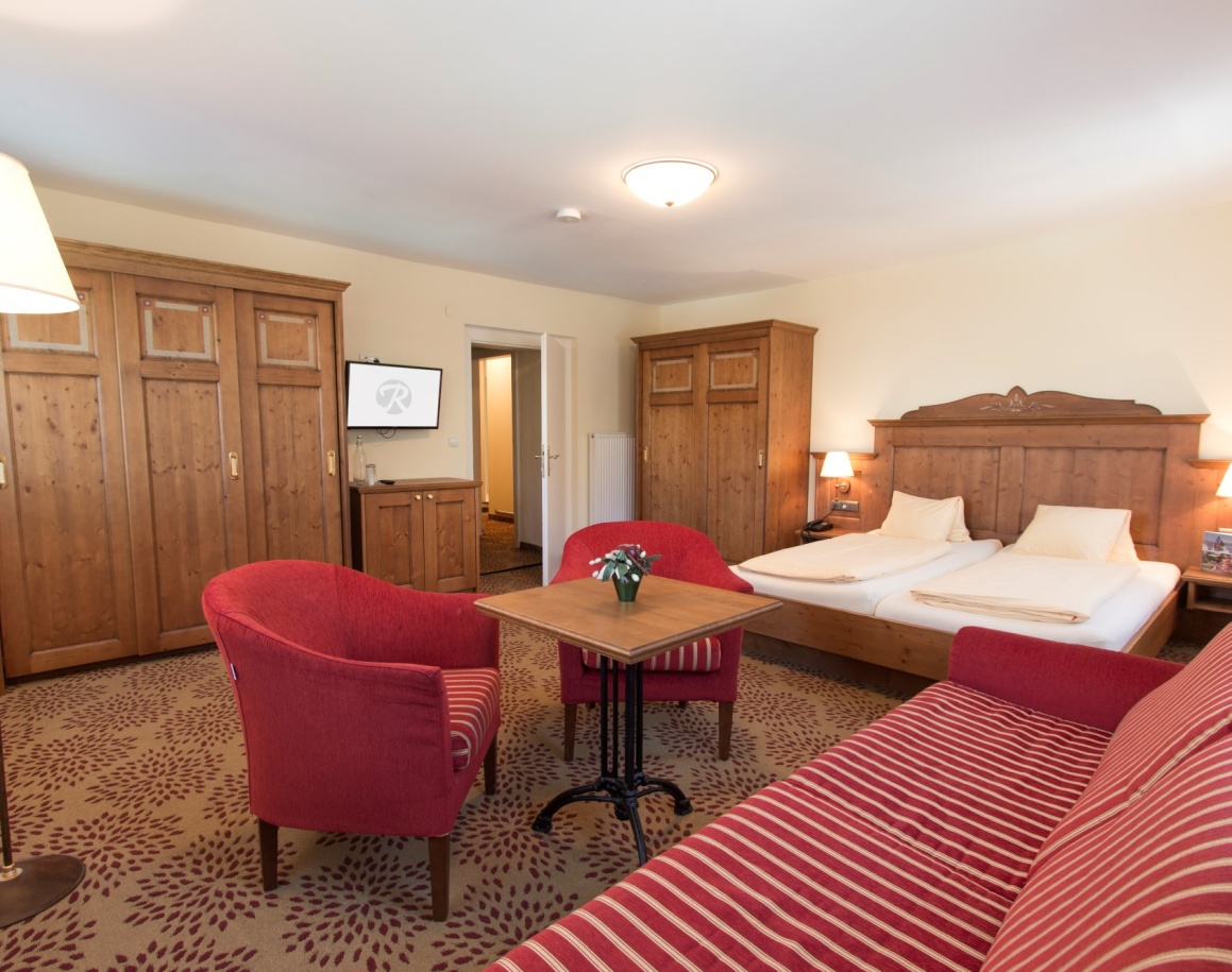 Gemütliches Hotelzimmer mit Doppelbett, roten Sesseln und Holzmöbeln