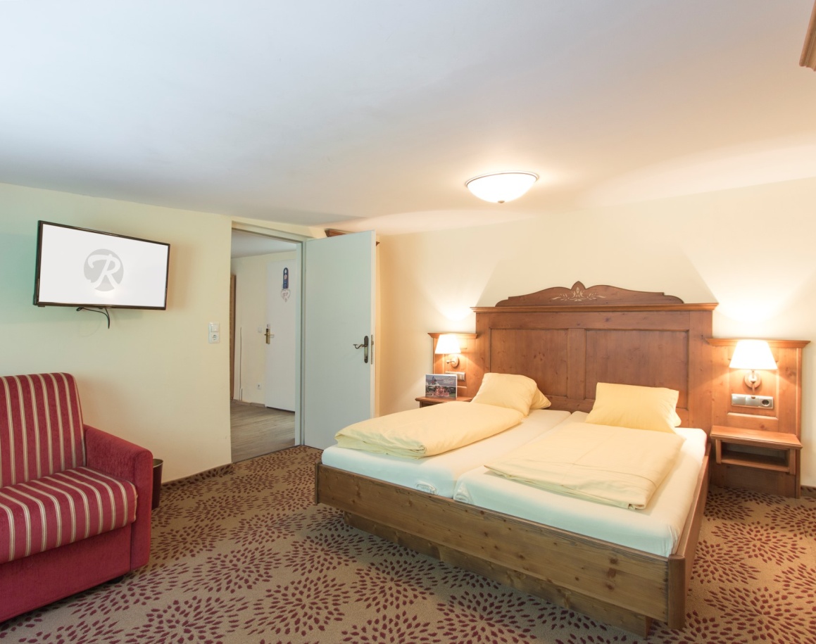 Schlafzimmer mit Doppelbett, rotem Sessel, Teppichboden und Fernseher an der Wand