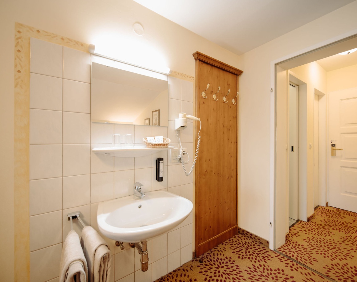 Ein helles Badezimmer mit Waschtisch, Spiegel, Handtüchern und Haartrockner an der Wand