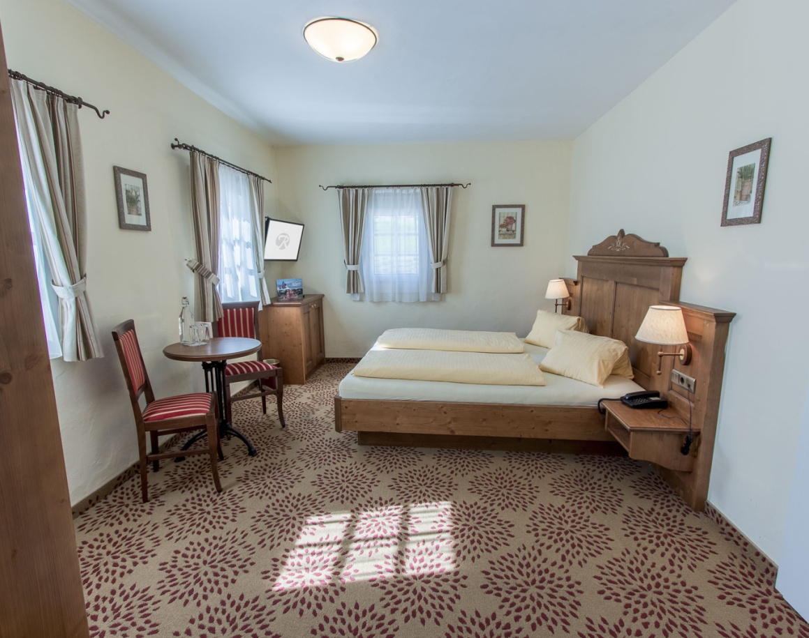 Helles Zimmer mit Doppelbett, gemustertem Teppich und zwei Stühlen