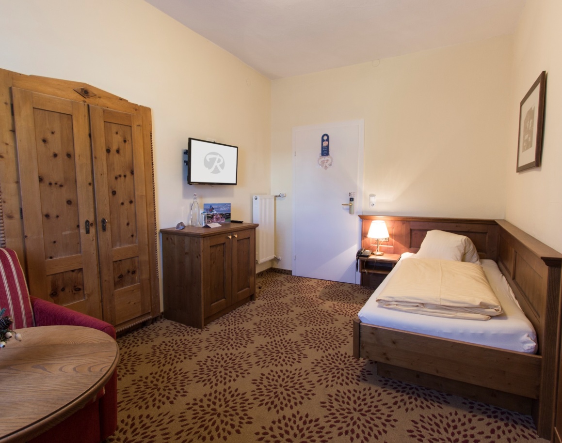 Einzelzimmer mit Holzmöbeln, Teppichboden und Nachttischlampe