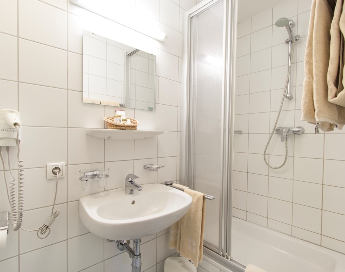 Helles Badezimmer mit Duschkabine, Waschbecken und Handtüchern an der Wand