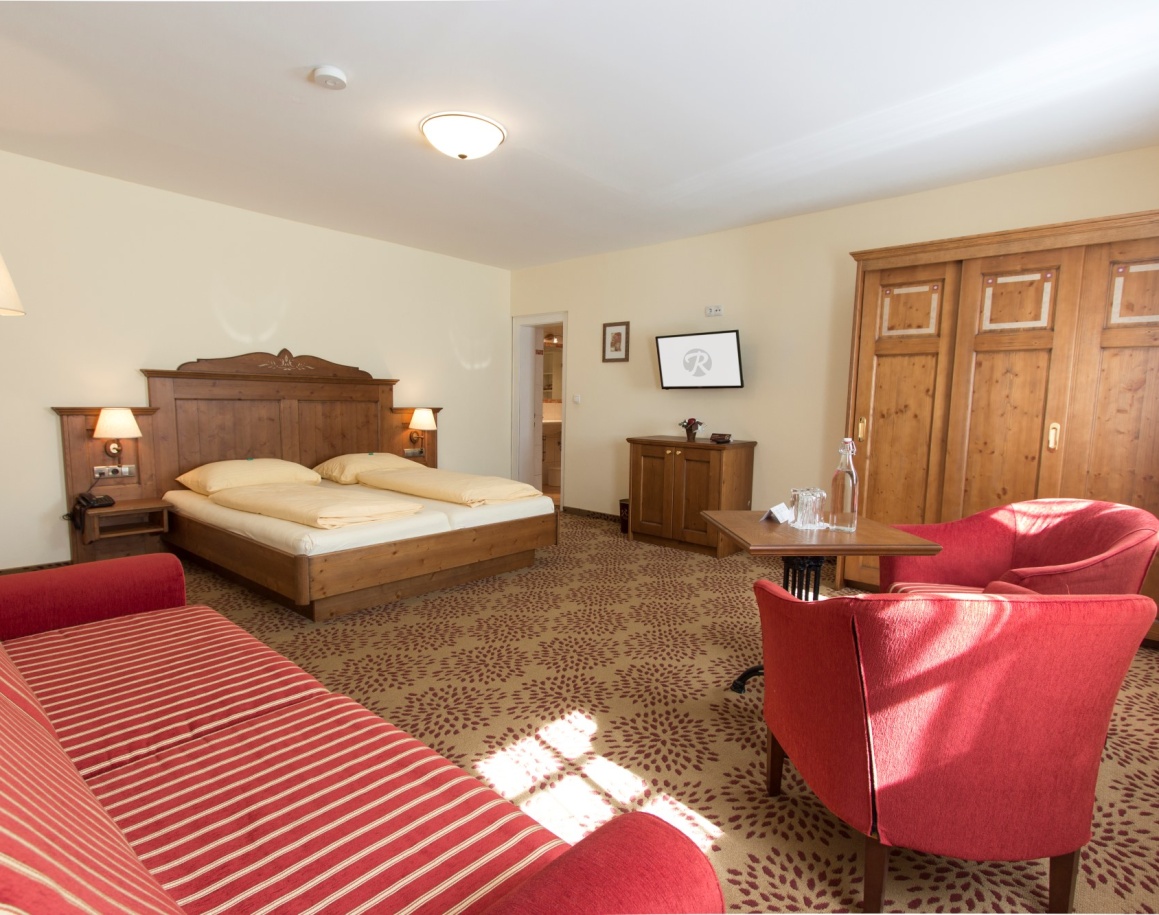 Geräumiges Hotelzimmer mit Doppelbett, roten Sesseln und Holzmöbeln