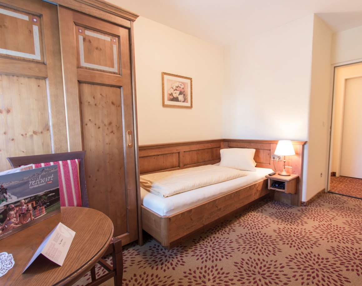 Zimmer mit Einzelbett, kleinem Tisch und Stehlampe