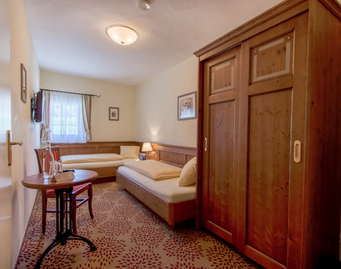 Gemütliches Hotelzimmer mit zwei Einzelbetten, Holzmöbeln und einem kleinen Tisch