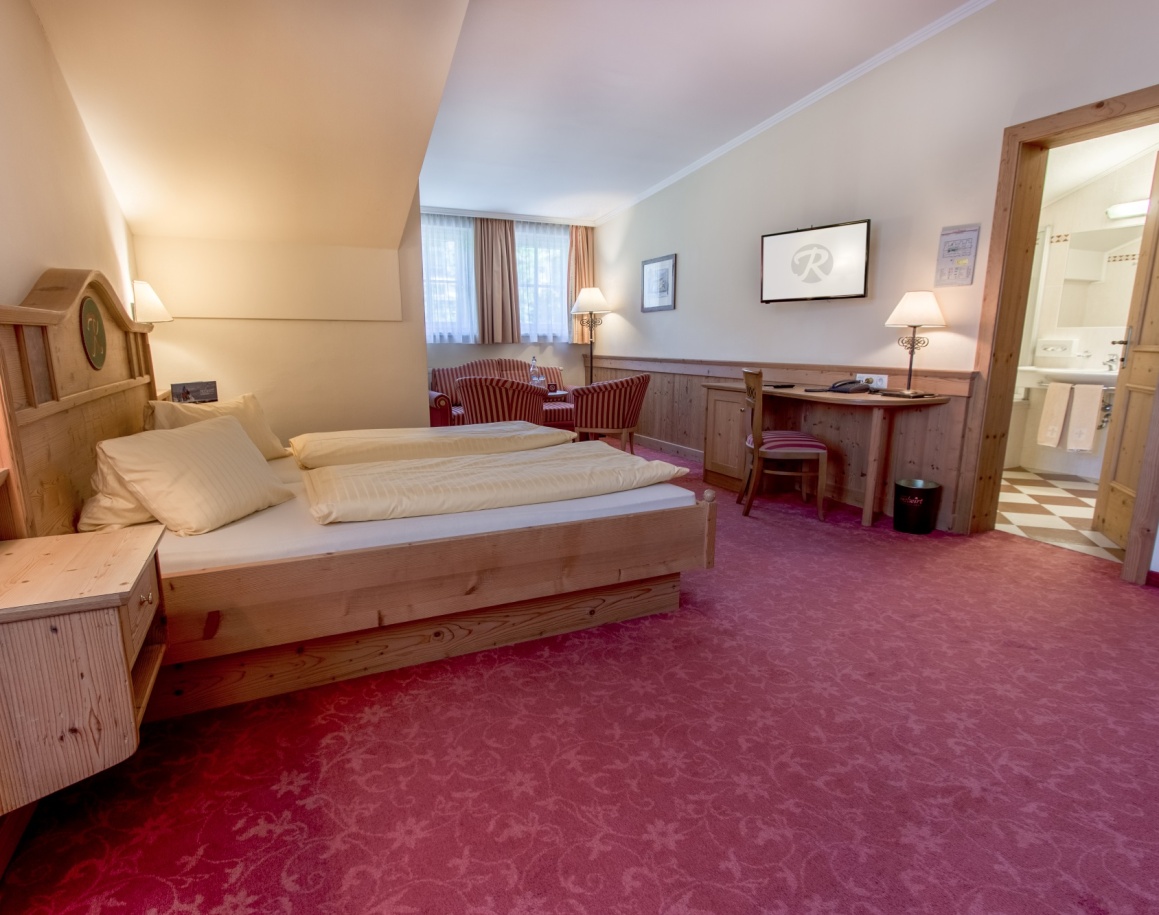 Hotelzimmer mit Doppelbett, Schreibtisch und großen Fenstern