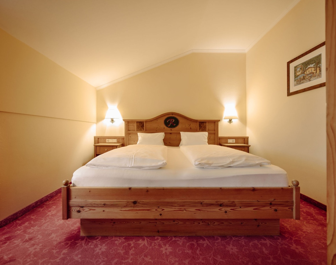 Hotelzimmer mit Doppelbett, Nachttischen und rotem Teppichboden