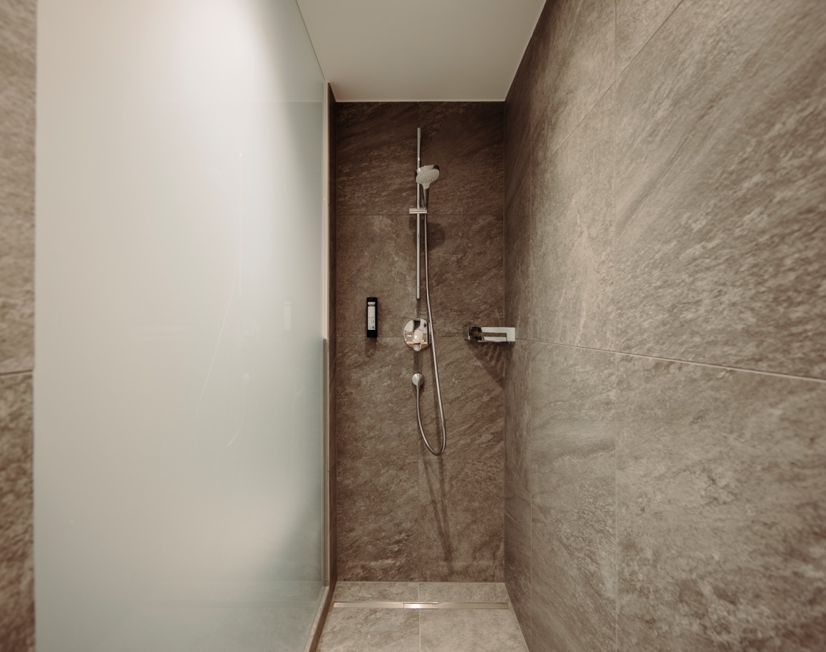 Hotelbadezimmer mit Dusche und grauen Fliesen